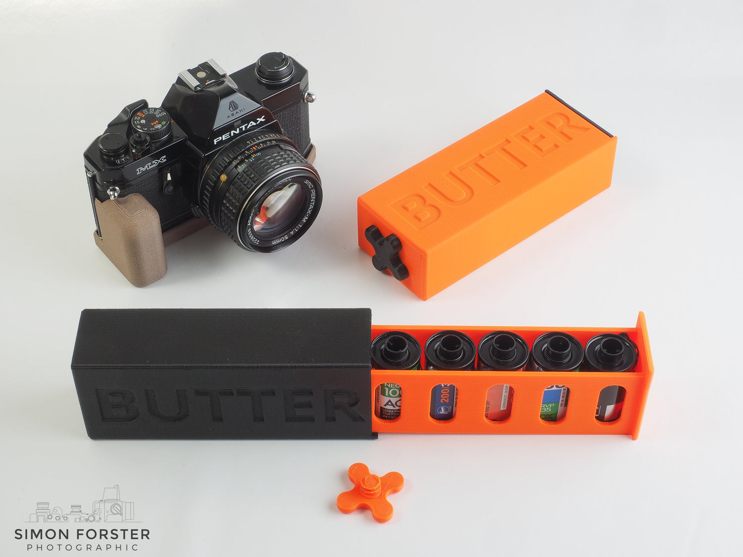 35mm BUTTER BOX Film Case by Cameradactyl in black and orange, with a Pentax MX camera displayed above.