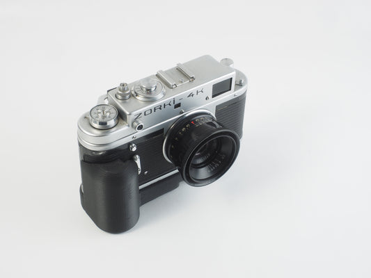 A Zorki 4K camera with a black grip attached to it, set against a white background.