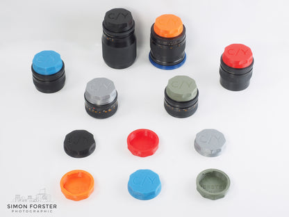 Assorted Contax/Yashica rear lens caps in various colours for Contax/Yashica mount lenses by Forster UK on white backdrop.