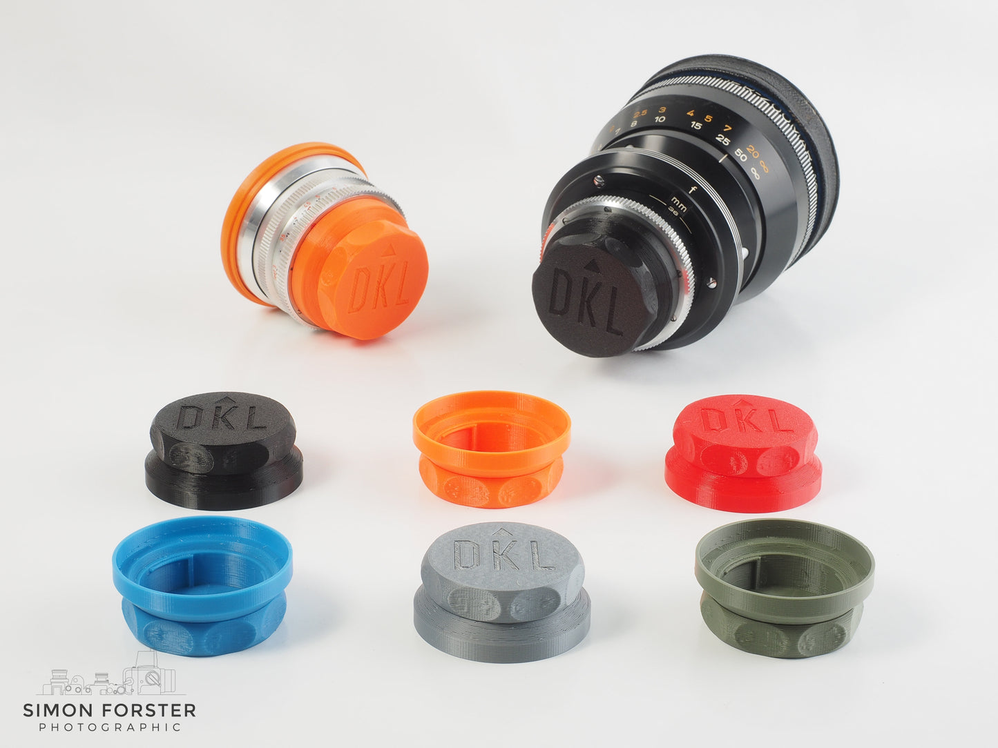 An orange DKL schneider rear lens cap has been fitted onto a DKL Schneider lens, and so is a black version of the cap, which has been fitted onto another DKL schneider lens. A range of colours are present aswell, such as red, blue, silver, and green.