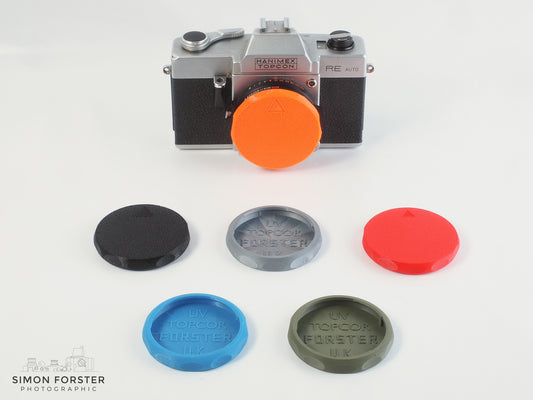 Six body caps have been designed to fit topcon cameras are being showcase within a simple plain white background. At the back there is a orange body cap which has been mounted onto a topcon camera. In front of the orange body cap and the camera, there are the other five caps which are in the colours, black, silver, red, mid blue and survival green.